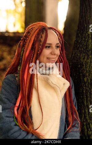 Porträt einer positiven jungen Frau mit Dreadlocks im Waldpark. Hübsche Hündin mit heller Frisur, die wegschaut und lächelt Stockfoto