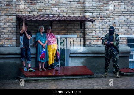 ©Michael Bunel / Le Pictorium/MAXPPP - Michael Bunel / Le Pictorium - 29/05/2014 - Ukraine / Donbass / Donetsk - Deux femmes et un homme s'abrigant de la pluie alors qu'un homme armes et cagoules se tient pres d'eux. Apres les combats a l'aeroport de Donetsk, des pro-russes auraient pille un supermarche. Les hommes du bataillon Vostok kommt quelques jours plutot seraient venus ce jour la pour arreter les responsables. Une Operation Visant a les deloger de l'OGA, le batiment de l'Administration regionale d'Etat, occupe depuis le Debut de l'Insurrection des separatistes etait en cours a ce mum Stockfoto