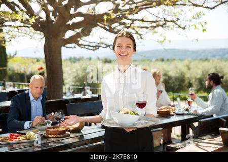 Positive Frau Kellner demonstrieren open-air Restaurant für Besucher Stockfoto