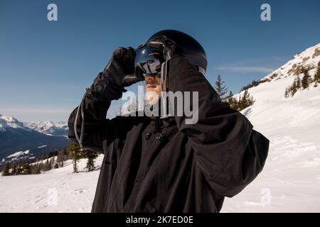 Junger männlicher Snowboarder, der seine Brille im sonnigen Skigebiet anpasst