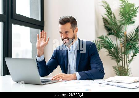 Fernes Online-Gespräch. Positiver kaukasischer Geschäftsmann, Geschäftsführer, der auf den Laptop-Bildschirm schaut und per Videokonferenz spricht, virtuelle Online-Meetings mit Kollegen führt und lächelt Stockfoto