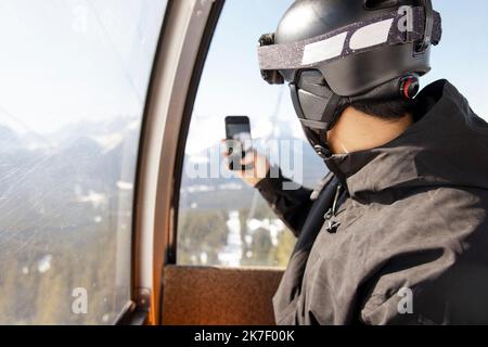 Junger männlicher Snowboarder mit Kameratelefon in der Skilift-Gondel