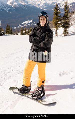 Porträtfreudiger junger männlicher Snowboarder auf der sonnigen Skipiste des Skigebiets