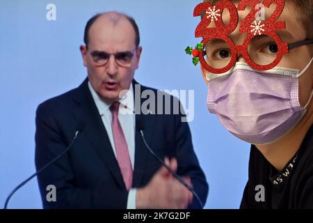 ©PHOTOPQR/L'EST REPUBLICAIN/ALEXANDRE MARCHI ; NANCY ; 27/12/2021 ; SANTE - POLITIQUE - OMICRON - EPIDEMIOLOGIE COVID 19 - CORONAVIRUS - CONFERENCE DE PRESSE PM - 5EME VAGUE - DOSE DE RAPPEL - JAUGE - DOSE DE RAPPEL - PASS SANITAIRE - PASS VACCINAL - REVEILLON JOUR DE L'AN. Dezember 27 in Nancy 2021. Une personne, portant un Masque chirurgical de Protection et des lunettes fantaisie pour le réveillon de la Saint Sylvestre 2022, regarde et écoute le Premier ministre Jean CASTEX lors d'une conférence de Presse télévisée à la Suite du conseil de défense sanitaire alors qu'une nouvelle vague de contaminina Stockfoto