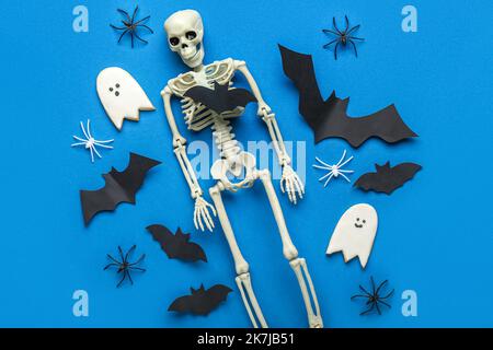 Papierfledermäuse mit Skelett, Halloween-Kekse und Spinnen auf blauem Hintergrund Stockfoto