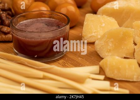 Verschiedene Sorten von Käse, Walnusskernen, geräucherten Wachteleiern und Honig in einer Glasvase auf einer Holzoberfläche. Stockfoto