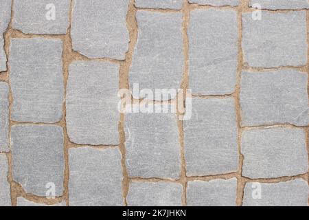 Textur des Fragments des grauen Pfades aus Mauerwerk mit Sand in Nähten zwischen Pflastersteinen. Draufsicht Stockfoto