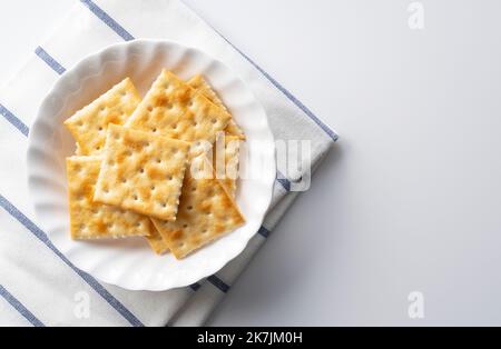 Viele Cracker auf einer Platte, die auf einem weißen Hintergrund mit Platz platziert ist. Blick von direkt oben. Stockfoto