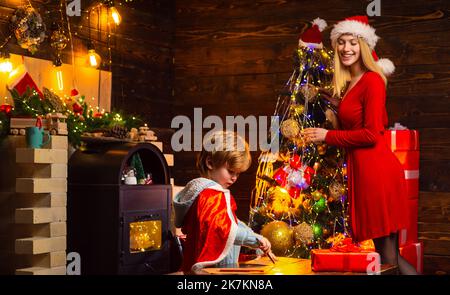 Portrait von glücklicher Mutter und entzückendes Baby, das Weihnachten feiert und einen Neujahrsbaum schmückt. Glückliches Familienpaar. Glückliche Kinderträume werden wahr Stockfoto