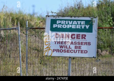 Ein Privateigentum, Gefahr, Hausfriedensbruch wird verfolgt Schild an einem Tor vor überwuchertem Gras und Sträuchern im Hintergrund angebracht werden Stockfoto