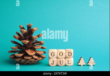 Kleine Holzblöcke mit der Aufschrift God Jul, Scandinavian Merry Christmas, türkisfarbener Hintergrund, minimalistische Weihnachtsdekoration aus Holz Stockfoto