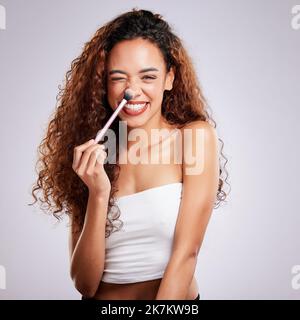 Werde kreativ mit Make-up. Eine junge Frau, die Make-up auf einem grauen Hintergrund aufgetragen hat. Stockfoto