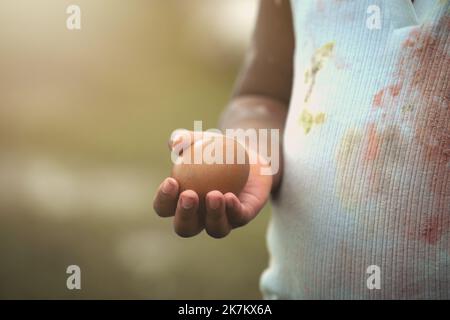 Afroamerikanisches Kind, das Hühnereier mit Farbfleck auf der Hand hält und sich kleidet. Stockfoto