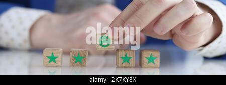 Der Kunde hält ein lächelndes Smiley-Gesicht auf dem Holzwürfel Stockfoto