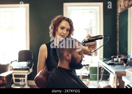 Ich bin fast fertig mit dir. Eine attraktive junge Friseurin, die in ihrem Salon die Haare ihrer Kunden styling. Stockfoto