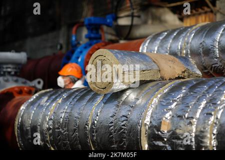 Details zur geringen Schärfentiefe (selektiver Fokus) mit industrieller Glaswolle, die zur thermischen Isolierung einer Heißwasser-Metallleitung verwendet wird. Stockfoto