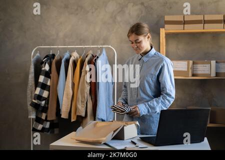 Online-Bestellung bis zur Auslieferung an den Kunden verpacken. Junge Frau bereitet Paketkasten mit Kleidung Produkt aus dem Online-Shop. Dropshipping Lieferung in e Stockfoto