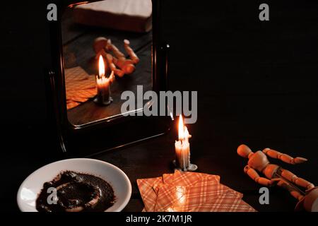 Eine brennende Kerze wurde von Spiegeln getragen und es gibt Wahrsagerkarten und Kaffeesatz auf einem Teller in der Nähe, Wahrsagerei auf Karten von Candleli Stockfoto