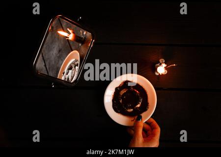 Eine brennende Kerze wurde von Spiegeln getragen und es gibt Wahrsagerkarten und Kaffeesatz auf einem Teller in der Nähe, Wahrsagerei auf Karten von Candleli Stockfoto