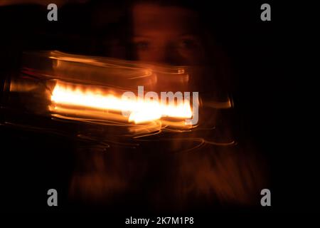 Ein junges ukrainisches Mädchen mit einer Petroleumlampe im Dunkeln sitzt zu Hause, ohne ein helles, langbelichtendes Foto in Bewegung zu haben Stockfoto