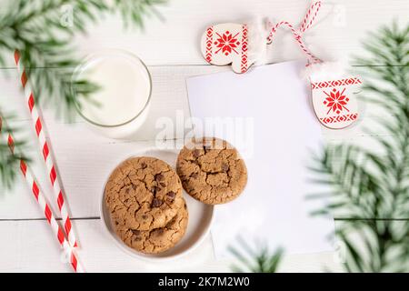 Weihnachtliche Anordnung aus Milchglas, Trinkhalmen, Keksen, leerem leerem leerem Blatt, dekorativ gemusterten Fäustlinge auf weißem Holztisch. Milch für den Weihnachtsmann. Draufsicht durch Stockfoto