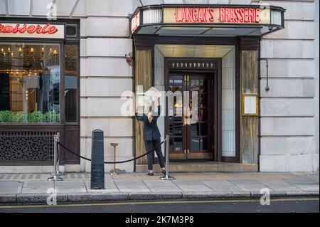 Junge Frau wechselt die Speisekarte im Außenbereich in Langan's Brasserie. Stratton Street, Mayfair, London, England, Großbritannien Stockfoto