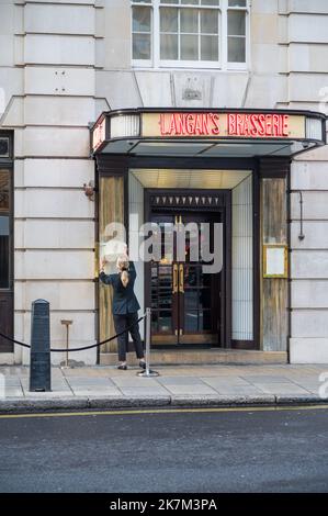 Junge Frau wechselt die Speisekarte im Außenbereich in Langan's Brasserie. Stratton Street, Mayfair, London, England, Großbritannien Stockfoto