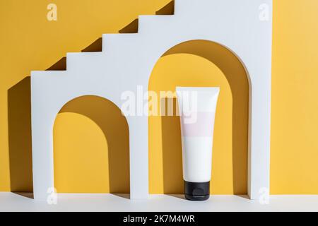 Beauty-Produktkonzept. Weiße Creme-Tube auf gelbem Hintergrund. Vorderansicht. Trendige Vitrine mit hartem Licht. Paket ohne Markenbezeichnung. Stockfoto