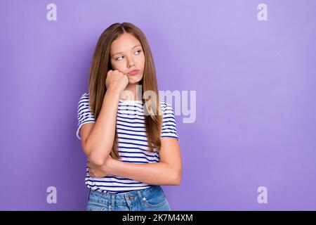 Foto von unzufrieden verärgert Mädchen gerade Frisur tragen gestreiften T-Shirt suchen leeren Raum Hand auf Wangenknochen isoliert auf lila Farbe Hintergrund Stockfoto