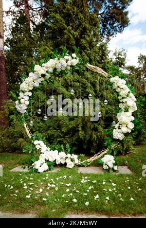 Hochzeitszeremonie. Sehr schöner und stilvoller Hochzeitbogen, geschmückt mit verschiedenen frischen Blumen, im Garten stehend. Hochzeitstag. Frische Blumen de Stockfoto