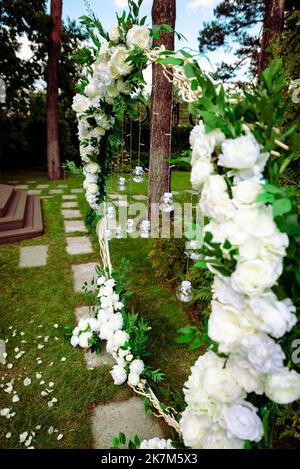 Hochzeitszeremonie. Sehr schöner und stilvoller Hochzeitbogen, geschmückt mit verschiedenen frischen Blumen, im Garten stehend. Hochzeitstag. Frische Blumen de Stockfoto