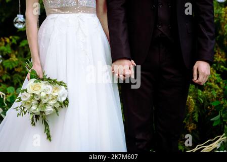 Die Braut hält einen Brautstrauß aus Rosen in den Händen, Hochzeitstag Blumen. Schöner Bohemian Hochzeit Blumenstrauß. Mädchen in einem Kleid mit einem Bouq Stockfoto