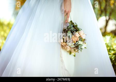 Die Braut hält einen Brautstrauß aus Rosen in den Händen, Hochzeitstag Blumen. Schöner Bohemian Hochzeit Blumenstrauß. Mädchen in einem Kleid mit einem Bouq Stockfoto