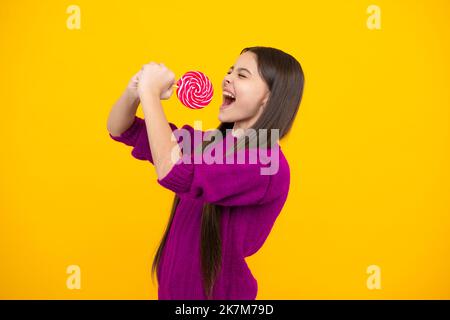 Aufgeregtes Gesicht. Hipster Teenager Kind Mädchen lecken Lollypop. Zucker Ernährung, Süßigkeiten und Süßigkeiten. Kind isst Lollipop-Popsicle. Erstaunlicher Ausdruck, fröhlich Stockfoto