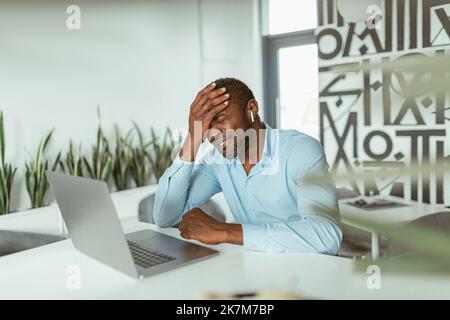 Müde afrikanischer Geschäftsmann, der auf einem Laptop sitzt und in einem modernen Coworking sitzt Stockfoto
