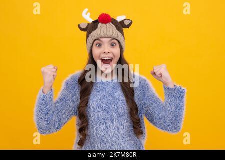 Schöne Winter Kinder Porträt. Teenager Mädchen posiert mit Winter Pullover und Strickmütze auf gelbem Hintergrund. Aufgeregtes Gesicht, fröhliche Emotionen von Stockfoto