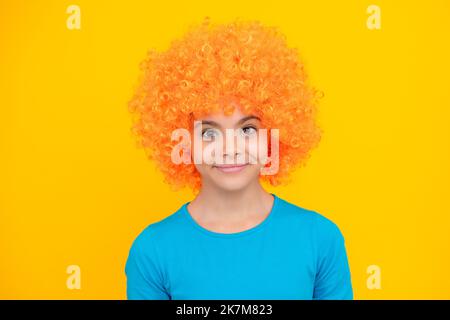 Lustiges Kind in lockiger Rothaarperücke. Zeit nach Viel Spaß. Teen Mädchen mit orangefarbenen Haaren, als Clown. Glückliches Teenager-Porträt. Lächelndes Mädchen. Stockfoto