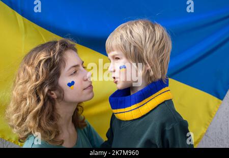 Junge und junge Frau mit gelb-blauem Herz auf den Wangen vor dem Hintergrund der ukrainischen Flagge. Familie, Einheit, Unterstützung. Kinder gegen Krieg. Anrufen Stockfoto