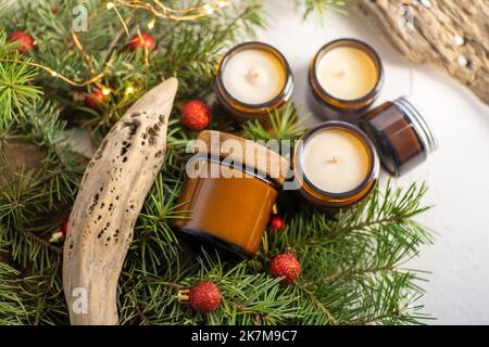 Sojalkerzen brennen in Gläsern. Komfort zu Hause. Kerze in einem braunen Glas. Duft und Licht. Handgemachte Duftkerze. Aromatherapie. Weihnachtsbaum und Winterstimmung. Gemütliche Einrichtung. Festliche Girlande-Dekoration Stockfoto