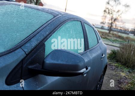 Ein Porträt eines gefrorenen Seitenspiegels und Seitenfenster eines komplett gefrorenen Autos während der Winterzeit. Das Eis muss zuerst schmelzen oder vor der Th entfernt werden Stockfoto