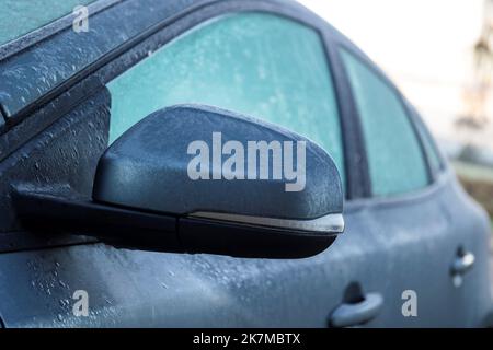 Ein Porträt eines gefrorenen Seitenspiegels eines vollständig gefrorenen Autos während der Winterzeit. Das Eis muss zuerst schmelzen oder entfernt werden, bevor der Fahrer die Sicherheit gewährleisten kann Stockfoto