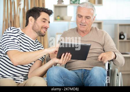 Fröhlicher behinderter Mann in der Nähe von hübscher Sohn, der Tablet anschaut Stockfoto