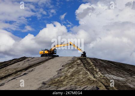 Gelber Raupenbagger auf der Baustelle auf einem großen Erdhaufen mit wunderschönem Himmelshintergrund. Stockfoto