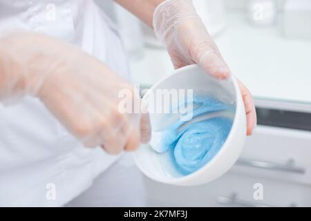 Schale mit blauer Alginatmaske in den Händen der Kosmetikerin. Stockfoto