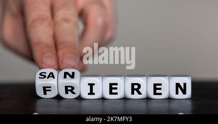 Die Hand dreht Würfel und ändert das deutsche Wort „frieren“ in „sanieren“. Stockfoto