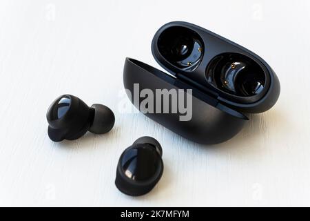 Schwarze kabellose Ohrhörer mit berührungslosem Aufladen in Nahaufnahme auf weißem Hintergrund. Box mit kabellosen Kopfhörern. Stockfoto