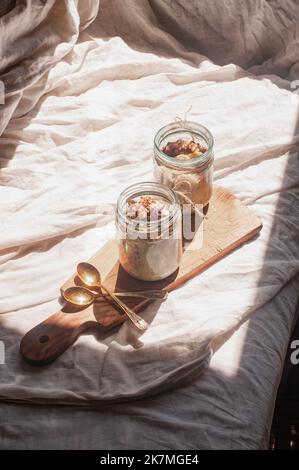 Köstlich über Nacht kein Koch vegane rohe rustikale Haferflocken in einem Glas mit Banane und Datteln auf minimalistischem sonnigen schönen neutralen beigen Hintergrund Stockfoto