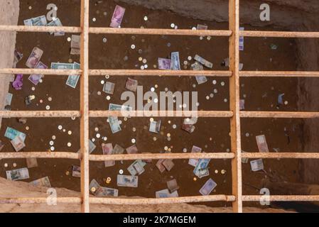 Verschiedene Münzen und Banknoten im Loch unter Eisenstangen. Touristen möchten Geld in der Großen Pyramide als Ritual für Glück oder Spende hinterlassen. Stockfoto