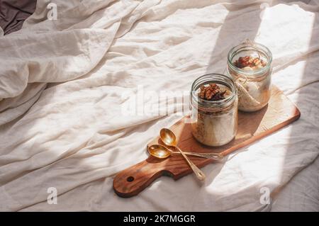 Köstlich über Nacht kein Koch vegane rohe rustikale Haferflocken in einem Glas mit Banane und Datteln auf minimalistischem sonnigen schönen neutralen beigen Hintergrund Stockfoto