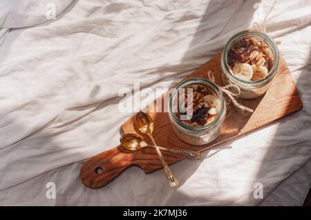 Köstlich über Nacht kein Koch vegane rohe rustikale Haferflocken in einem Glas mit Banane und Datteln auf minimalistischem sonnigen schönen neutralen beigen Hintergrund Stockfoto